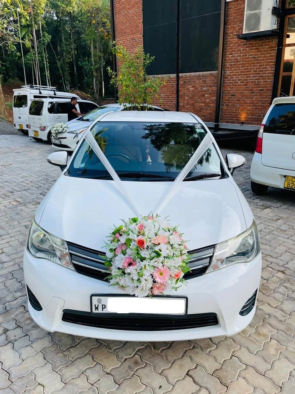 White sedan with a circular white and peach floral bouquet on the grille and white ribbons